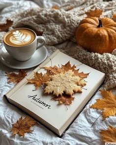 there is a cup of coffee and a book on the bed with autumn leaves around it