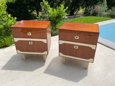 two wooden chests sitting next to each other on concrete near a swimming pool with trees and bushes in the background