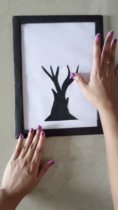 two hands are holding up a shadow of a deer on a white paper with black frame