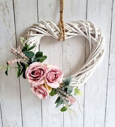 a heart shaped wreath with pink roses and greenery hangs on a white wooden wall