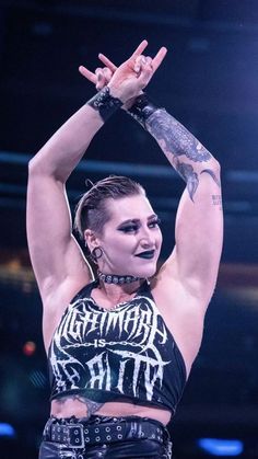 a woman with tattoos and piercings on her arm is holding up her hands in the air