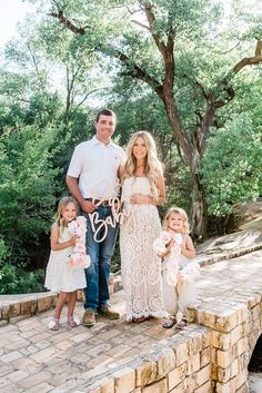 a couple and their two children posing for a photo on a brick wall with trees in the background