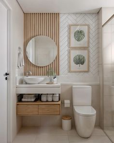 a white toilet sitting next to a bathroom sink under a round mirror on top of a wooden cabinet