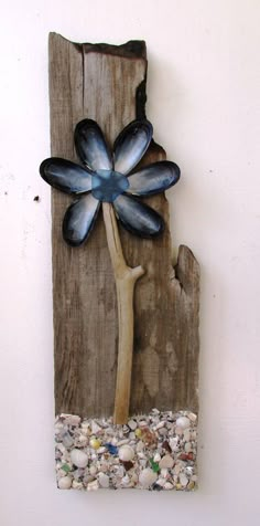 a piece of wood with a blue flower on it and shells in the ground below