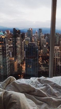 a view of a city from a high rise window in a hotel room with an unmade bed