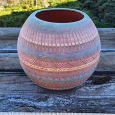 a large vase sitting on top of a wooden table next to a garden area with trees in the background