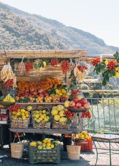 an outdoor fruit stand with fruits and vegetables on display in front of a mountain range