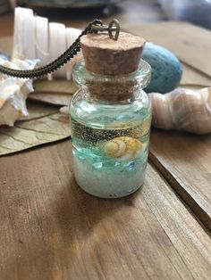 a bottle filled with sand and sea shells sitting on top of a wooden table next to seashells