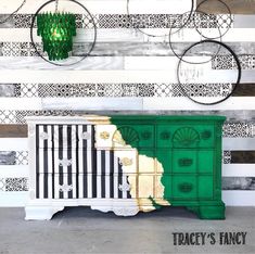 an old dresser painted green and gold with black and white stripes on the wall behind it