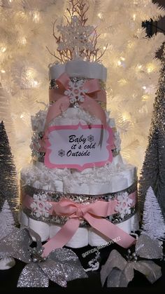 a three tiered cake decorated with pink and white ribbons, snowflakes and trees