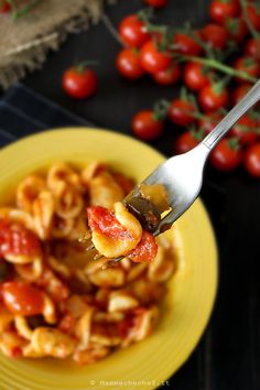 a fork full of pasta with tomato sauce on it and tomatoes in the back ground