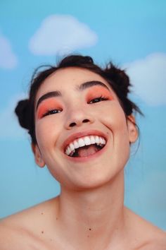 a woman with orange eyeshadow smiling and looking up at the sky above her head