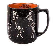 a black and orange coffee mug with skeletons on it, happy halloween written across the bottom