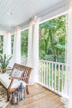 the porch is decorated with white curtains and wood furniture, along with a bench that has two lanterns on it