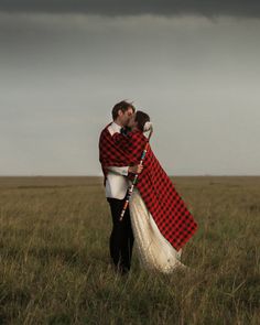 a man and woman dressed in traditional scottish clothing standing in a field under a stormy sky