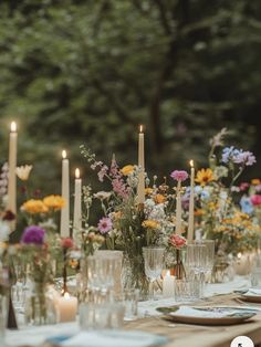 a long table with candles and flowers in vases on top of it, surrounded by greenery