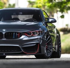 the front end of a gray bmw car parked on a street with trees in the background