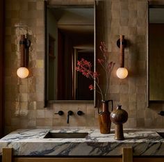 a bathroom with marble counter tops and two vases on the sink, along with mirrors