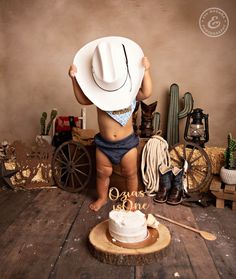 a small child wearing a cowboy hat and diaper standing in front of a cake