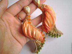 a pair of orange and green earrings on someone's finger with gold trimmings