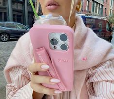 a woman holding a pink cell phone case in front of her face and drinking from a cup