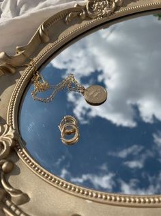 a mirror reflecting the sky and clouds with gold chains hanging from it's sides