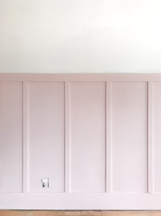 an empty room with white paneling and wood flooring on the wall, in front of a light switch