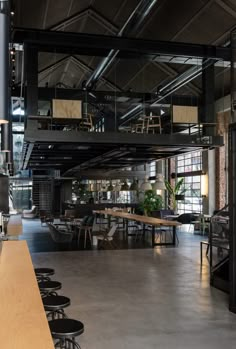 an industrial looking restaurant with tables and stools in the foreground, along with large windows