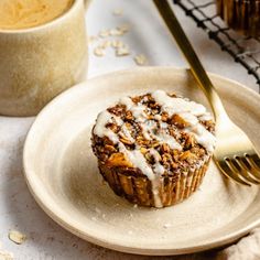 a muffin with icing on a plate next to a fork and cupcake