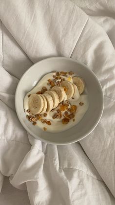 a white bowl filled with bananas and granola on top of a bed covered in sheets