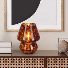 a brown vase sitting on top of a wooden table next to a framed art piece