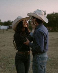 a man and woman in cowboy hats talking on their cell phones while standing in an open field