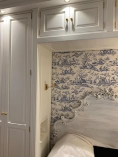 a white bed sitting next to a wall with blue and white wallpaper on it