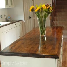 a vase filled with yellow and purple flowers on top of a wooden countertop in a kitchen