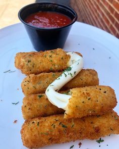 some deep fried food on a white plate with sauce and ketchup in a bowl