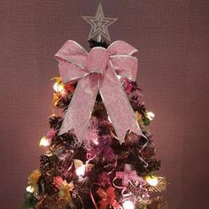 a small christmas tree decorated with pink and silver ribbons, lights and bows on top