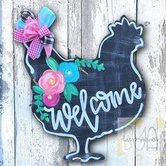 a welcome sign painted on the side of a wooden fence with flowers and a bow