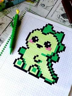 a green pixel art piece sitting on top of a white paper next to a pen