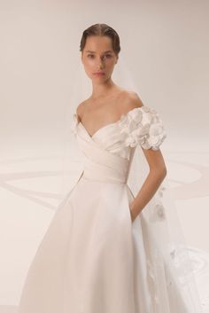 a woman in a white wedding dress with flowers on her shoulder and veil over her head