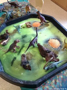 a tray filled with dinosaurs and plants in water