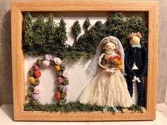 a wooden frame with two dolls in it and flowers around the couple's heads