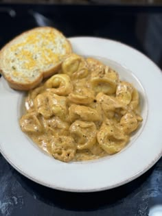 a white plate topped with macaroni and cheese next to a piece of bread