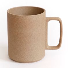 a coffee cup sitting on top of a white table next to a brown mug with handles