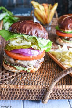 two hamburgers with lettuce, tomato and onion on a wicker tray