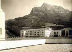 an old black and white photo of a building in front of a large mountain range