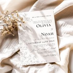 a white wedding card on top of a bed next to some dried flowers and sheets