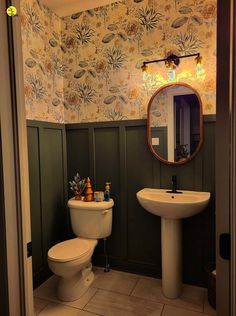 a bathroom with a toilet, sink and mirror in it's corner next to a wallpapered wall