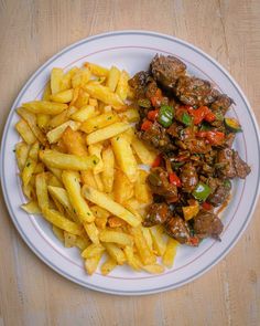 a white plate topped with french fries and meat covered in sauce on top of a wooden table