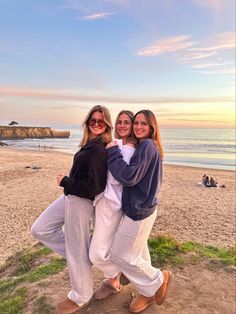 three women standing together on the beach at sunset with their arms around each other and smiling