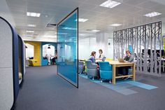 an office with people working on their laptops and sitting at desks in front of glass partitions